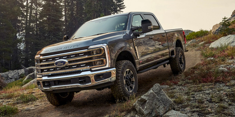 A Ford Super Duty truck driving off-road through a rugged, forested terrain.